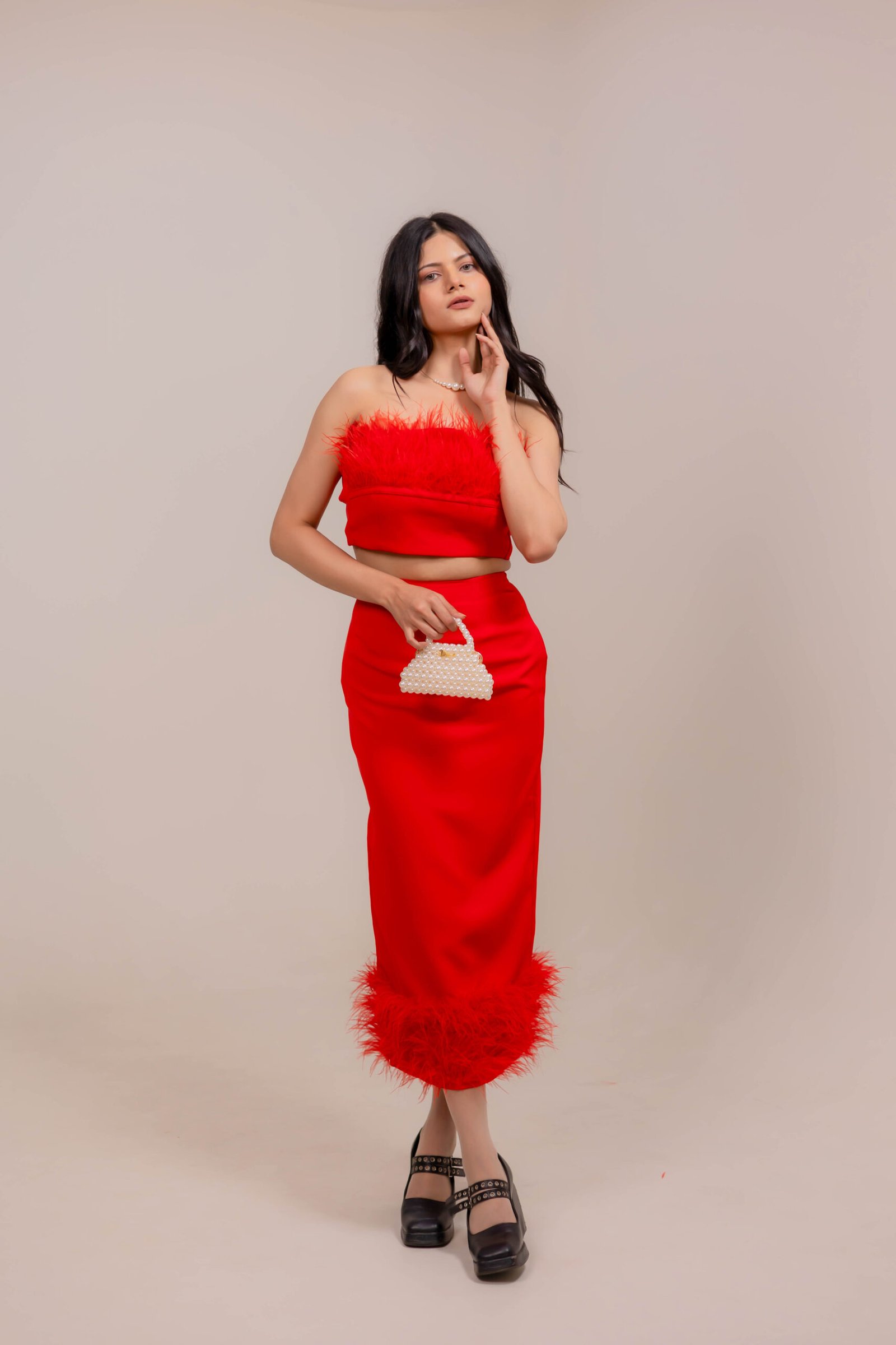 Full-length fashion portrait captured at Lens Grove Studio, a professional photo and video shoot rental space in Delhi, featuring a female model in a red dress holding a beaded handbag, styled against a minimal neutral backdrop with soft studio lighting for editorial and portfolio photography.