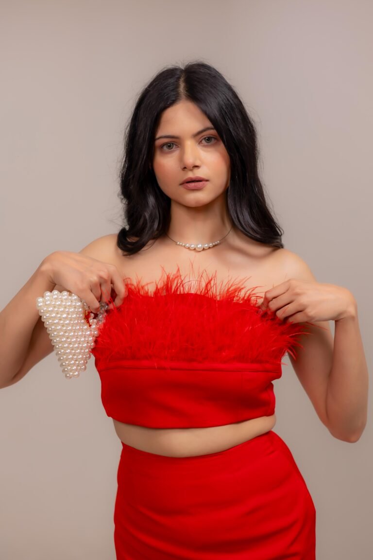 Studio fashion portrait shot at Lens Grove Studio, a professional photo and video shoot rental space in Delhi, featuring a female model in a red dress with a pearl heart-shaped handbag, posed confidently against a neutral backdrop with soft, even lighting for editorial and portfolio photography.