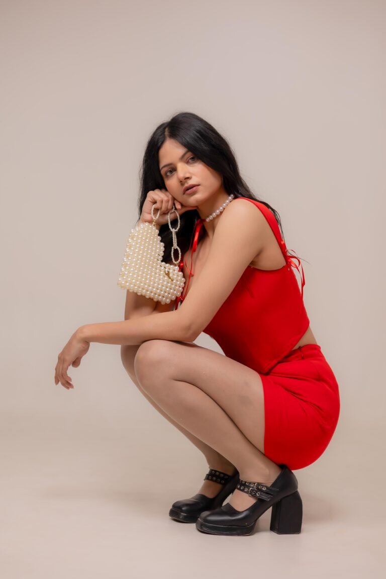 Fashion portrait shot at Lens Grove Studio, a professional photo and video shoot rental space in Delhi, featuring a female model wearing a red outfit and black heels, posing against a clean neutral background with soft studio lighting for editorial and portfolio photography.