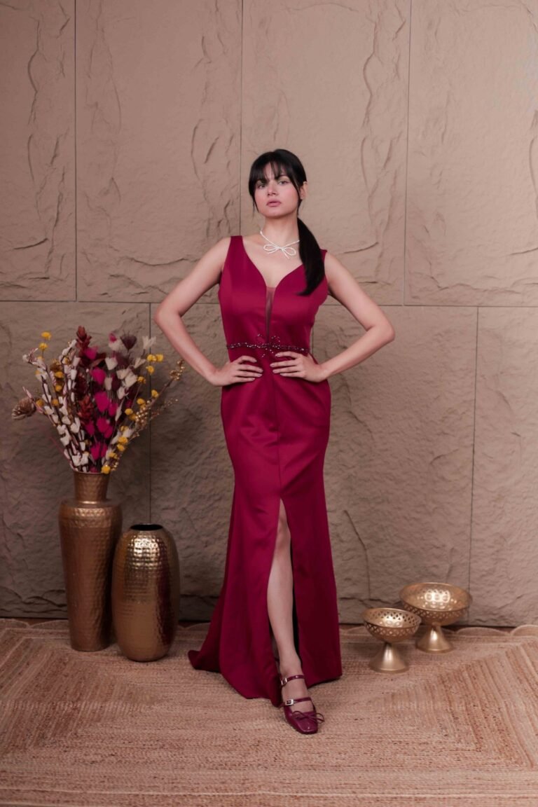 Editorial fashion portrait shot at Lens Grove Studio, a professional photo and video shoot rental space in Delhi, featuring a female model wearing a deep red gown, standing confidently against a textured neutral backdrop with warm cinematic lighting, styled for fashion, portfolio, and brand photography.