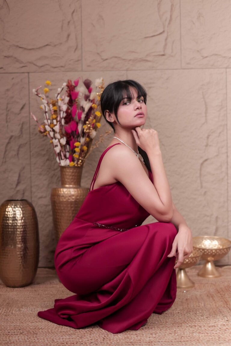 Editorial fashion portrait shot at Lens Grove Studio, a professional photo and video shoot rental space in Delhi, featuring a female model wearing a deep red gown, standing confidently against a textured neutral backdrop with warm cinematic lighting, styled for fashion, portfolio, and brand photography.