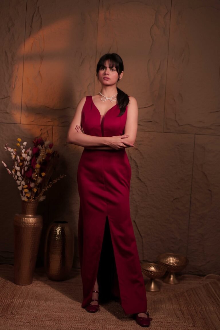 Editorial fashion portrait shot at Lens Grove Studio, a professional photo and video shoot rental space in Delhi, featuring a female model wearing a deep red gown, standing confidently against a textured neutral backdrop with warm cinematic lighting, styled for fashion, portfolio, and brand photography.