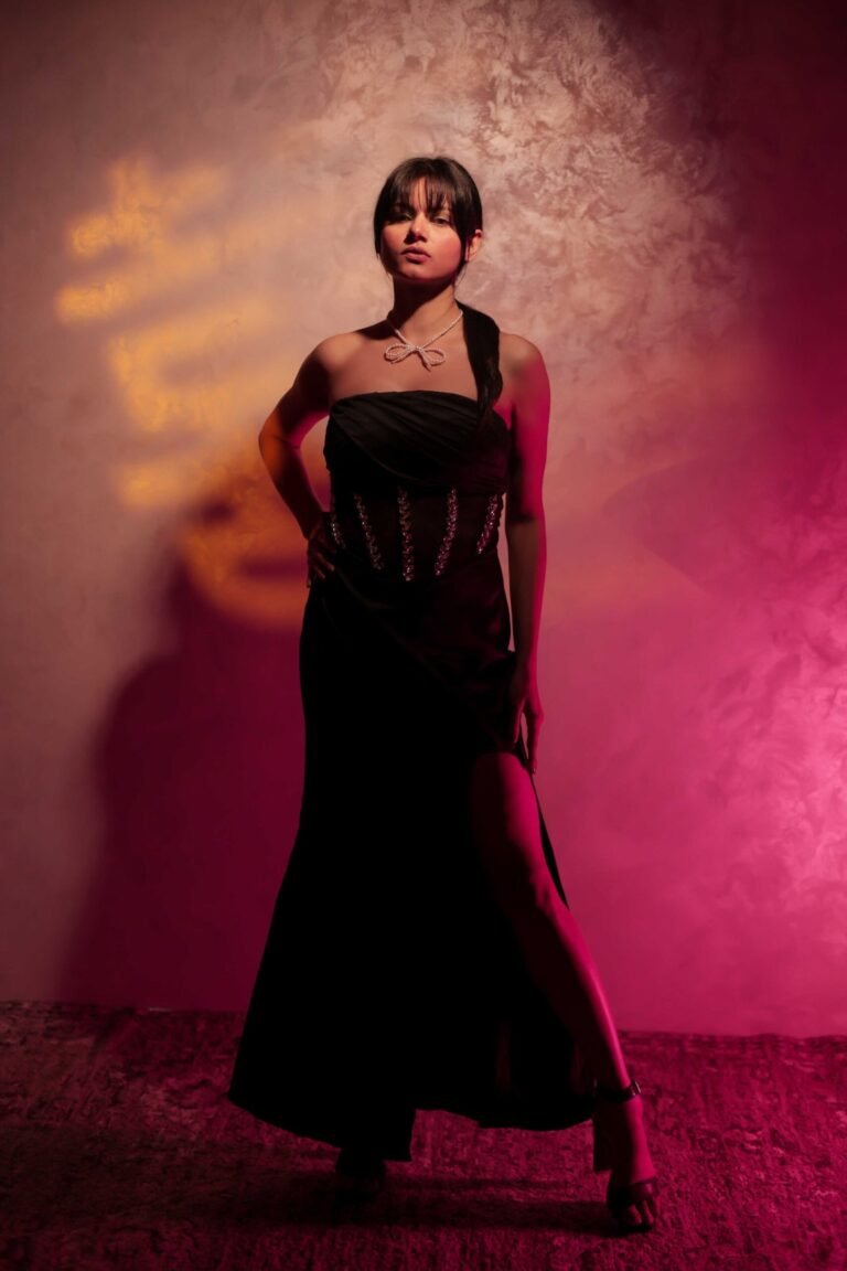 Dramatic fashion portrait captured at Lens Grove Studio, a professional photo and video shoot rental space in Delhi, featuring a female model in a black evening dress posed against a textured backdrop with bold red and warm spotlight lighting, showcasing cinematic studio lighting for editorial and portfolio photography.