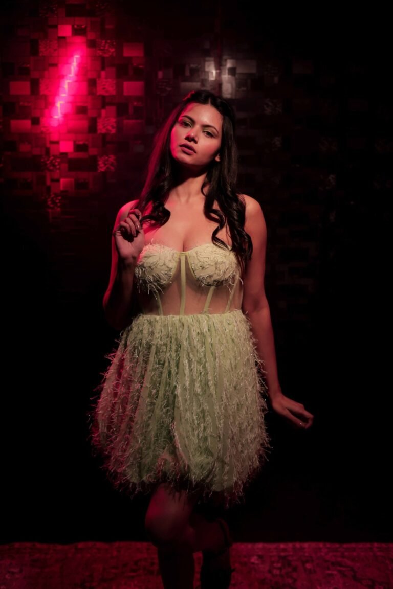 Cinematic fashion portrait shot at Lens Grove Studio, a professional photo and video shoot rental space in Delhi, featuring a female model in a light green textured dress, posed against a dark patterned backdrop with dramatic studio lighting for editorial and portfolio photography.