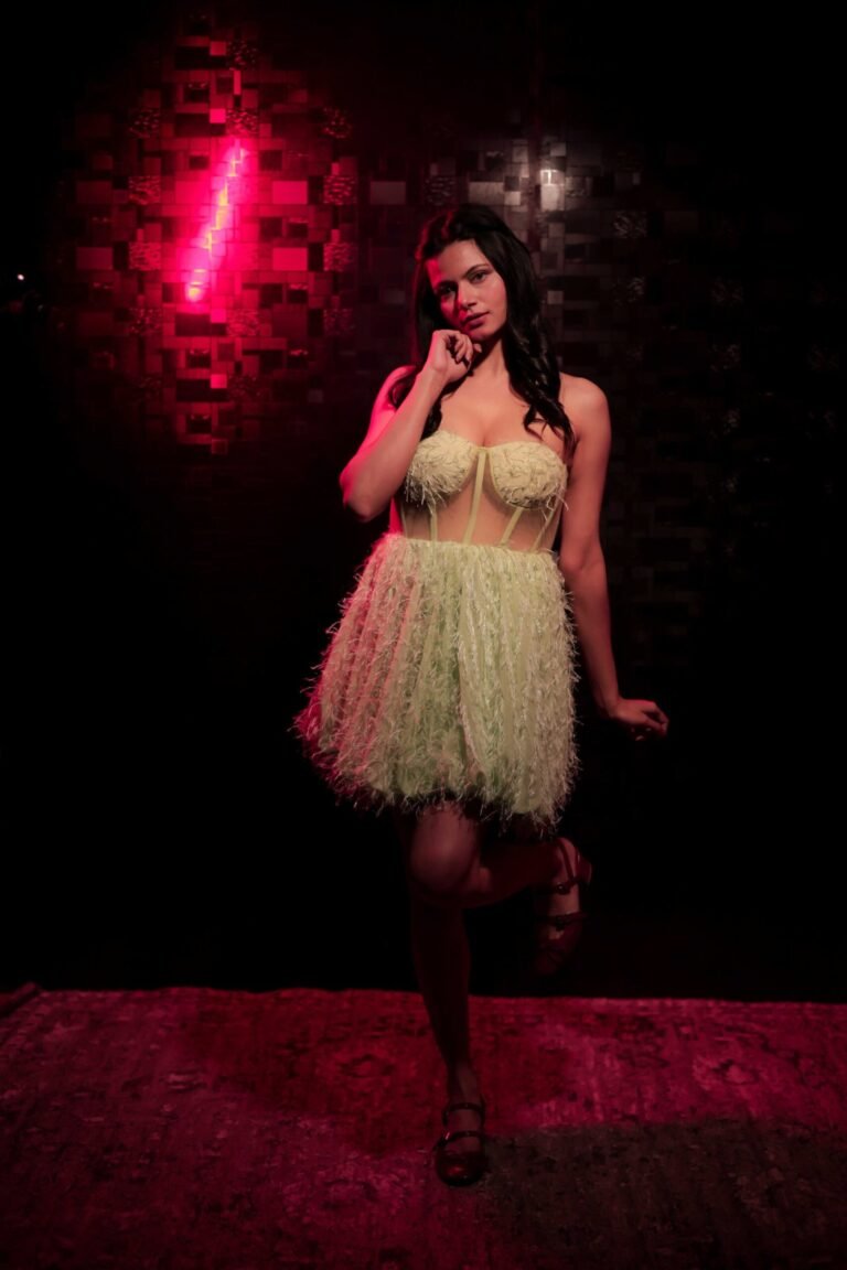 Cinematic fashion portrait shot at Lens Grove Studio, a professional photo and video shoot rental space in Delhi, featuring a female model in a light green textured dress, posed against a dark patterned backdrop with dramatic studio lighting for editorial and portfolio photography.