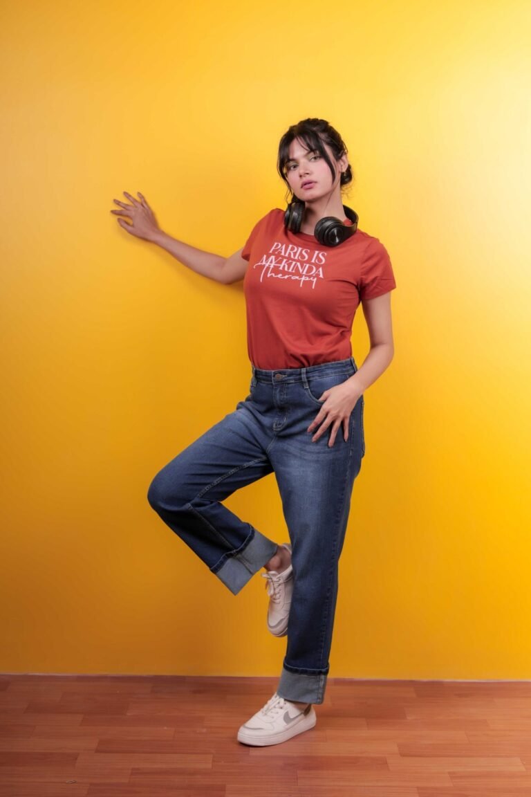 Casual fashion portrait shot at Lens Grove Studio, a professional photo and video shoot rental space in Delhi, featuring a female model wearing a graphic t-shirt, denim jeans, and sneakers, posing against a bold yellow backdrop with clean studio lighting for lifestyle and editorial photography.