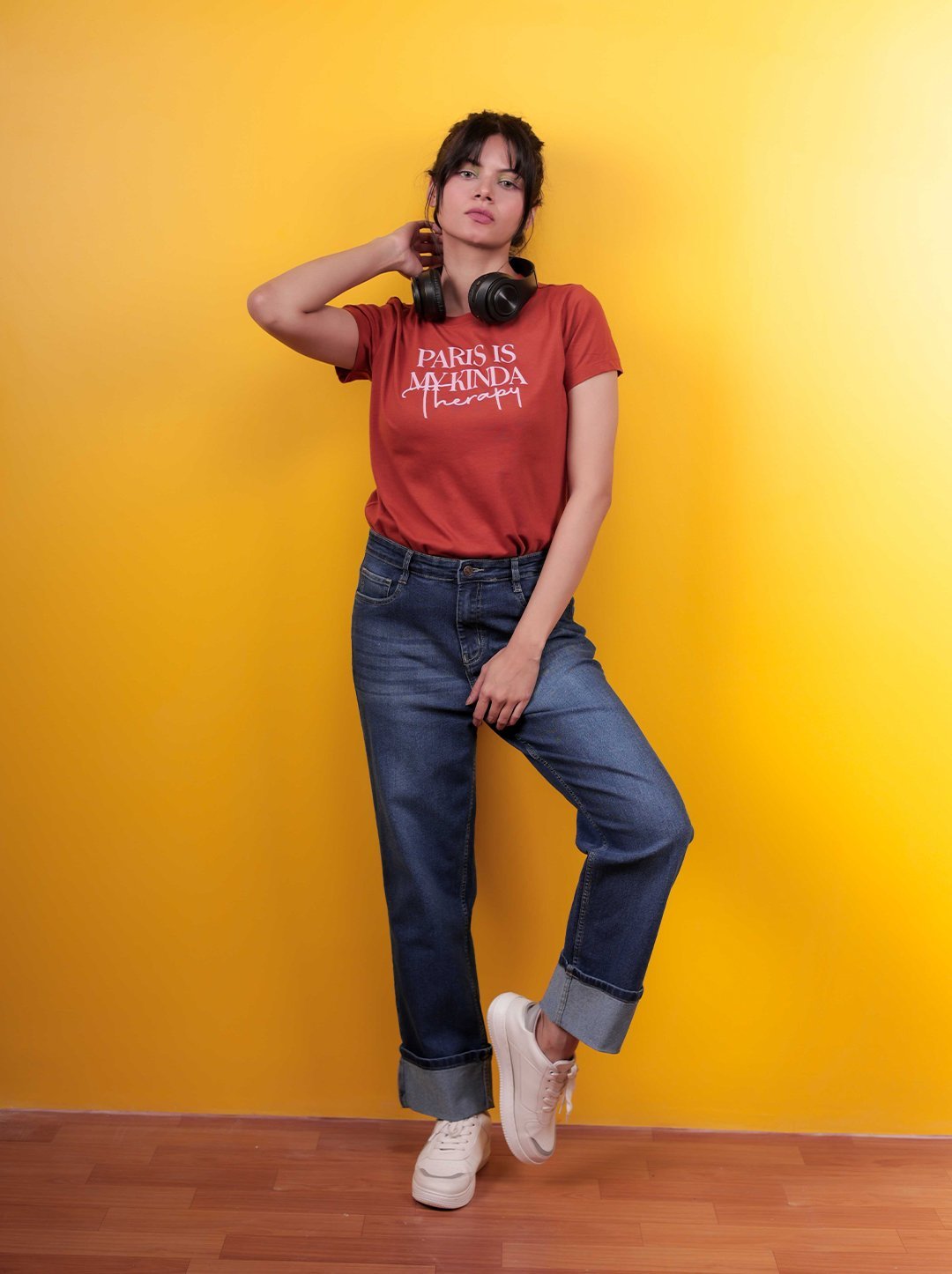 Casual fashion portrait shot at Lens Grove Studio, a professional photo and video shoot rental space in Delhi, featuring a female model wearing a graphic t-shirt, denim jeans, and sneakers, posing against a bold yellow backdrop with clean studio lighting for lifestyle and editorial photography.