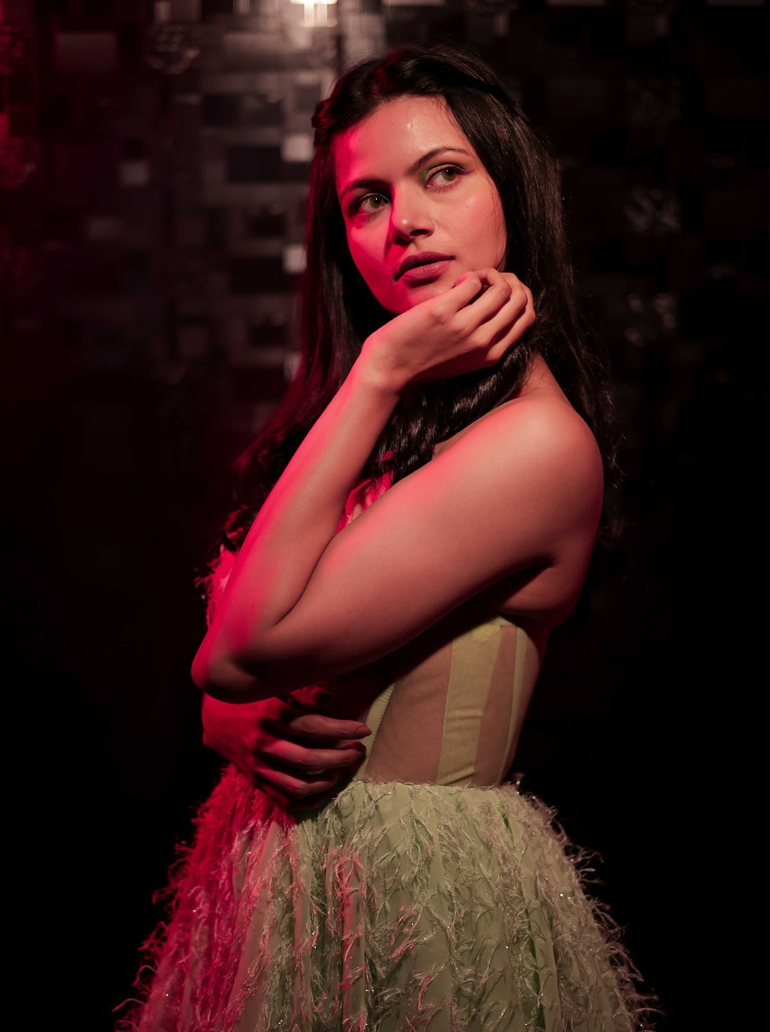 Dramatic fashion portrait shot at Lens Grove Studio, a professional photo and video shoot rental space in Delhi, featuring a female model in an evening dress illuminated with cinematic red lighting against a dark textured background, showcasing creative studio lighting for editorial and portfolio photography.